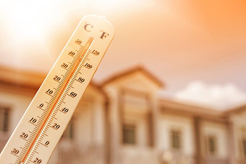 Termómetro marcando temperatura alta frente a una casa bajo el sol