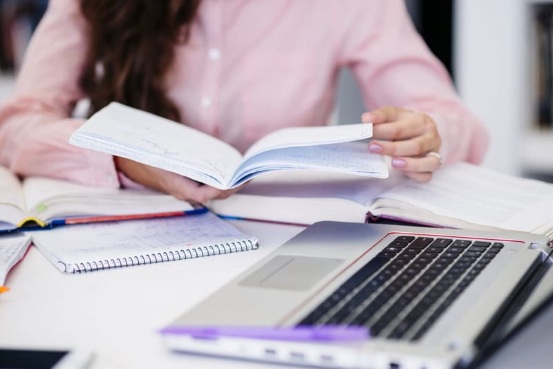 Estudiante leyendo un libro junto a su laptop y sus libretas