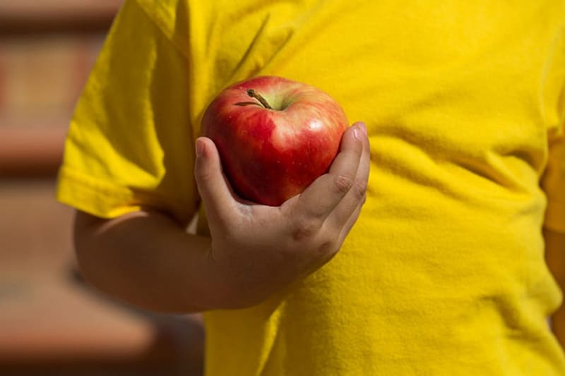 Niño con playera amarilla sosteniendo una manzana roja