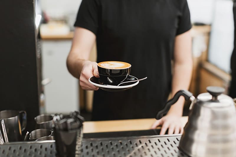 Barista entregando una taza de café con arte latte