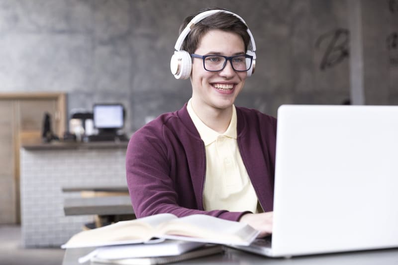 Joven con audífonos sonriendo mientras estudia en su laptop