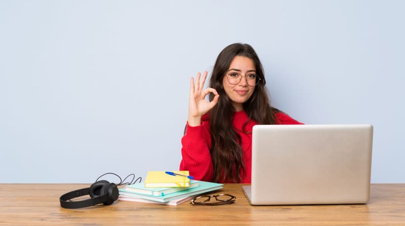 Estudiante sonriente haciendo una señal de OK frente a su laptop